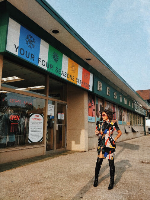 VINTA Mock Neck Tulip Terno Dress - Styled with Over-the-Knee Black Boots, Model Posing Outdoors by Storefront